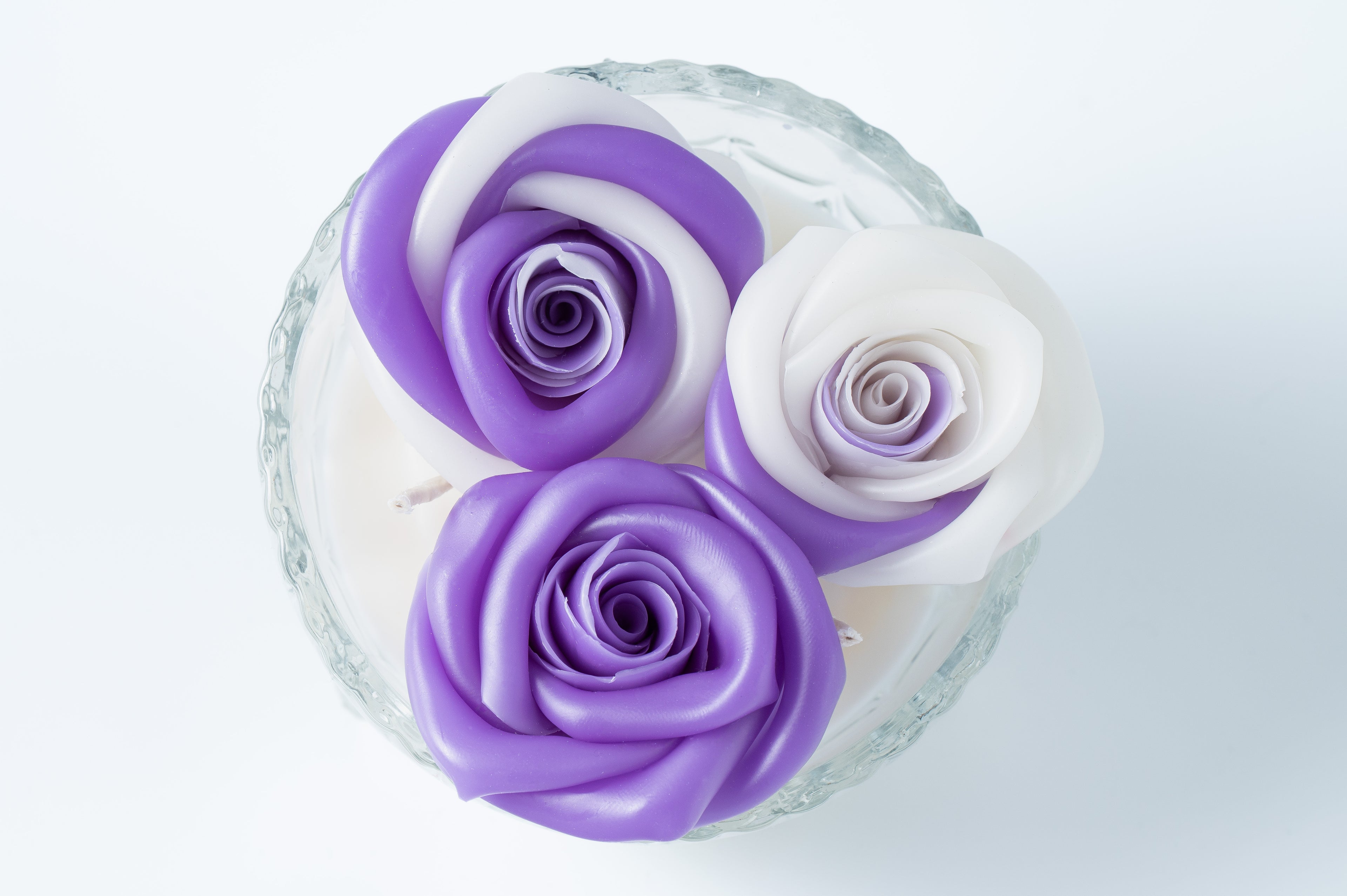 Candle with three purple and white roses in a clear glass vase on a light background