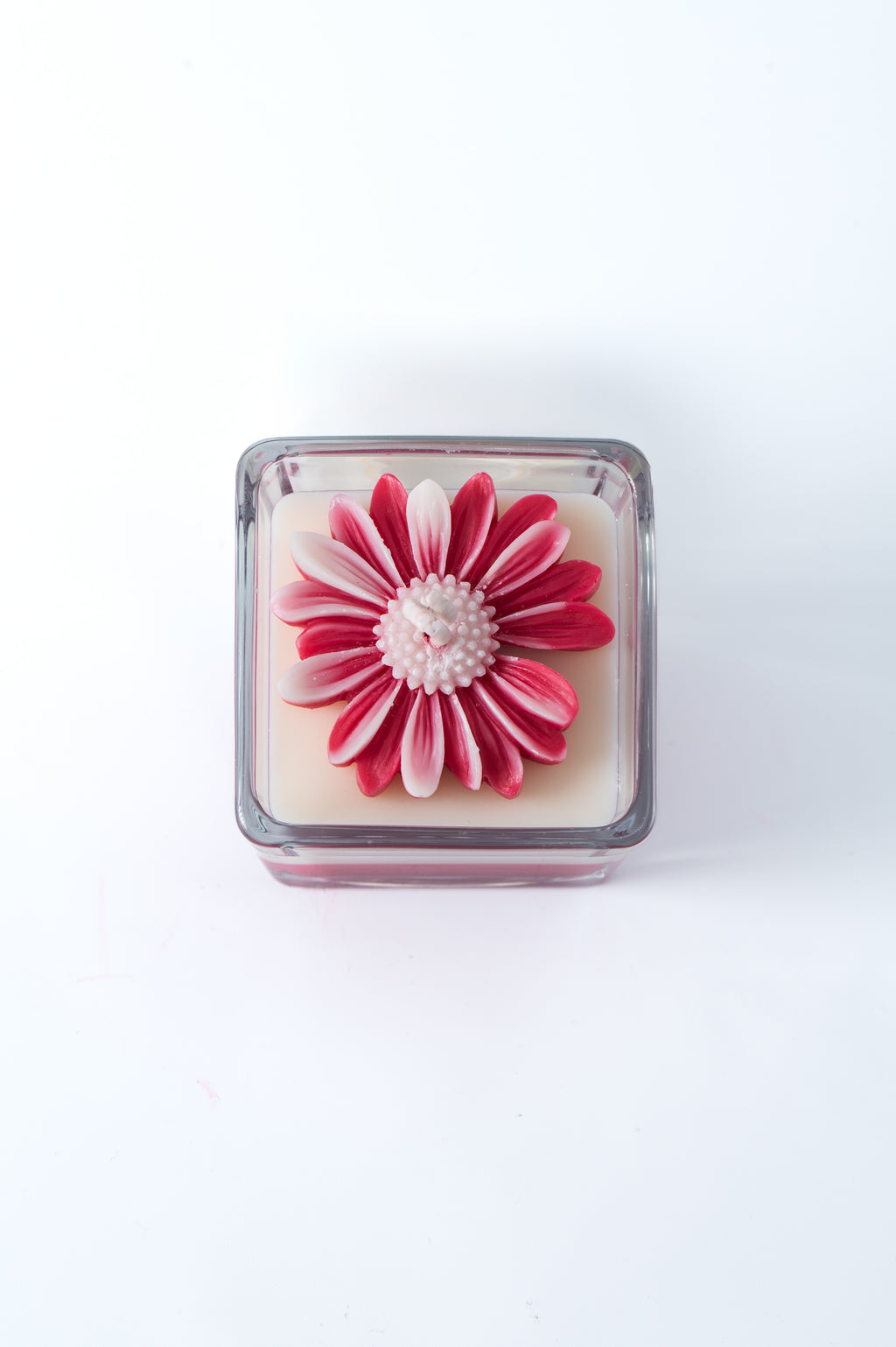 lumânare handmade în pahar pătrat din sticlă, cu floare roz din ceară și design în straturi alb și roz
