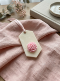 Odorizant parfumat din ceara in forma hexagonală decorat cu un bujor roz din ceara si panglica satinata roz, așezat pe masa