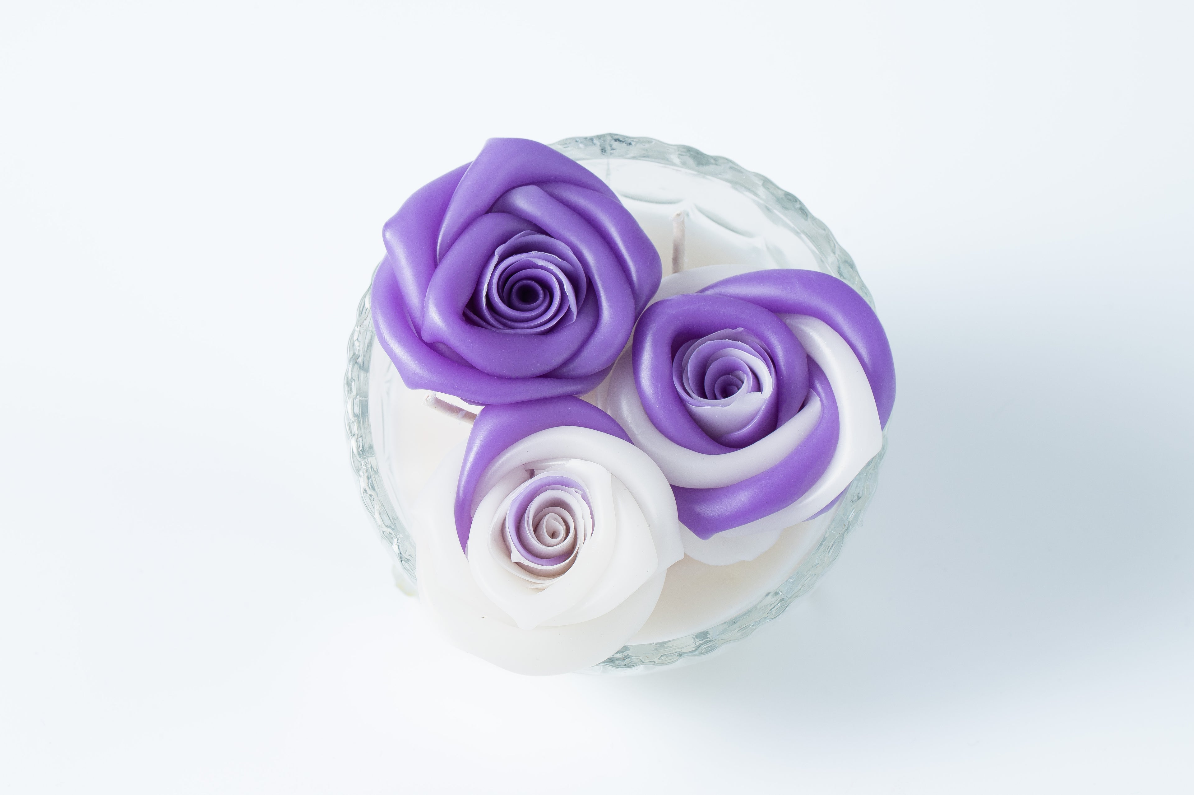 Candle with three purple and white roses in a clear glass vase on a light background