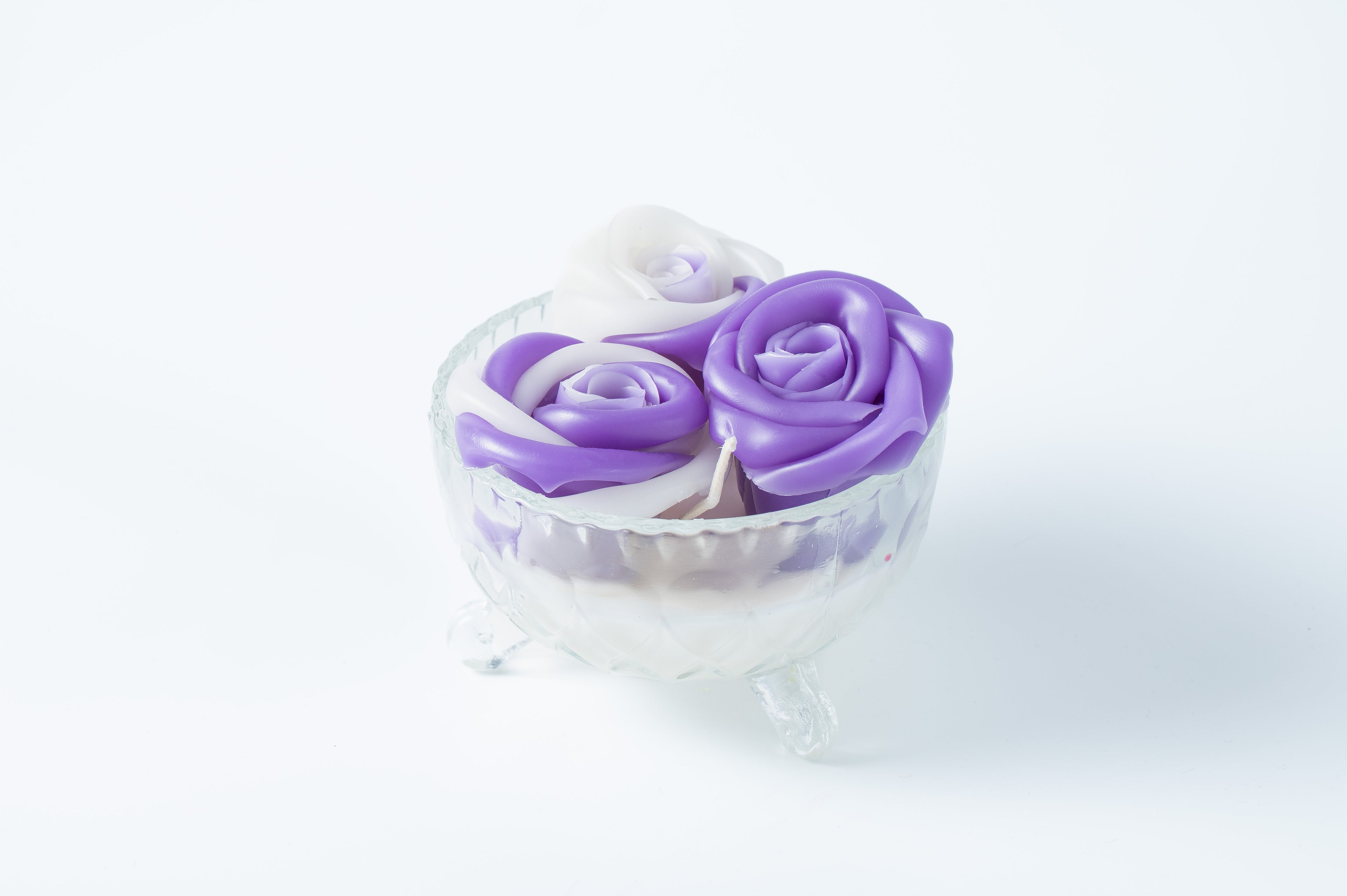 Candle with three purple and white roses in a clear glass vase on a light background